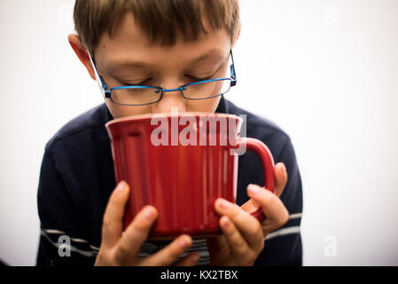 Un jeune garçon boit dans une tasse de thé dans une tasse rouge. Banque D'Images