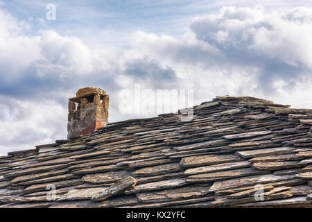 Toit en ardoise ; toiture en tuiles en pierre et cheminée contre ciel nuageux Banque D'Images