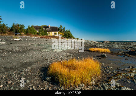 Une petite maison blanche et jaune de touffes de végétation sur la rive de la rivière Saint Laurent au Parc National du Bic à marée basse Banque D'Images