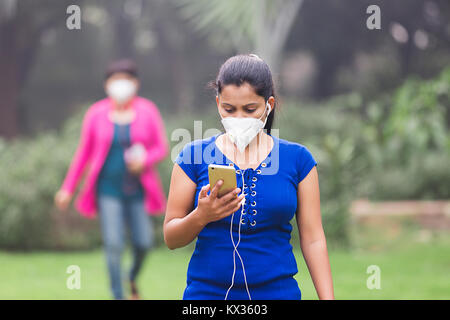 Jeune femme Musique Téléphone Mobile Oreillettes Pollution Park Banque D'Images