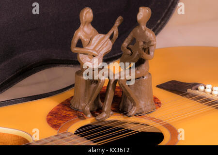 Model homme et femme assis, joueurs de guitare ensemble. Ornement de métal / memento peint en brun, en appui sur la plaque de travail d'une guitare acoustique. Banque D'Images