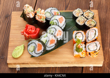 Une plaque de bois maintenant différents types de morceaux de sushis et rouleaux. servant des sushis sur une plaque de bois avec du gingembre et wasabi. La nourriture japonaise. Banque D'Images