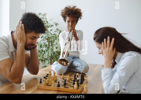 La mère et le père essayant de jouer aux échecs pendant que leur enfant joue trompette Banque D'Images