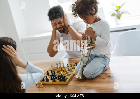 La mère et le père essayant de jouer aux échecs pendant que leur enfant joue trompette