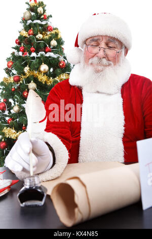 Santa Claus sitting at desk, écrit une liste de tous les garçons et les filles qui auront des cadeaux de Noël , isolé sur fond blanc Banque D'Images