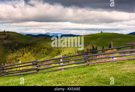 Clôture en bois sur une pente gazonnée de Carpathian alpes. Belle vue sur les champs sur les collines rurales. crête de montagne aux cimes enneigées au loin. Joli cou Banque D'Images