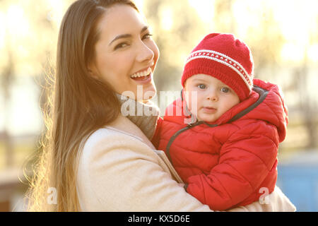 Portrait d'un smiley mère posant avec son bébé au chaud portant une veste rouge à l'extérieur en hiver Banque D'Images