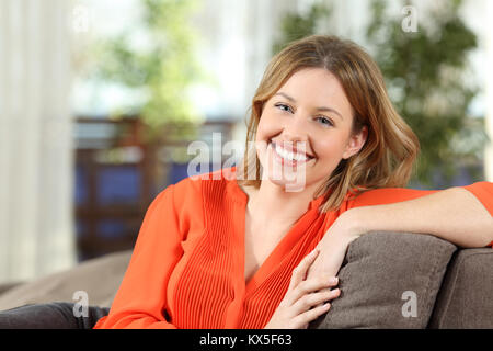 Vue avant portrait of a happy beauté blonde avec un sourire parfait qui pose sur un canapé dans la salle de séjour à la maison Banque D'Images