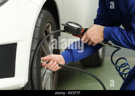 Close up d'un mécanicien de voiture mains contrôle de l'air des pneus avec un manomètre Banque D'Images