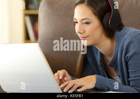 Fille watchng videos avec un ordinateur portable et un casque allongé sur un canapé dans la salle de séjour à la maison Banque D'Images