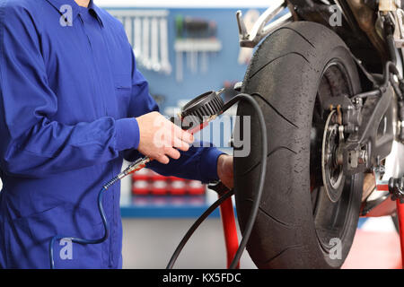 Close up d'un mécanicien moto part Contrôle des pneus air avec un manomètre dans un atelier Banque D'Images