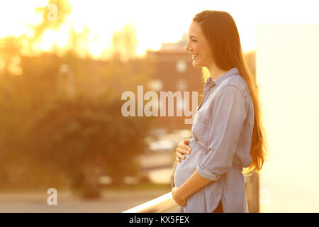 Vue latérale du portrait d'une femme enceinte à la suite pensif dans une chambre balcon au coucher du soleil Banque D'Images