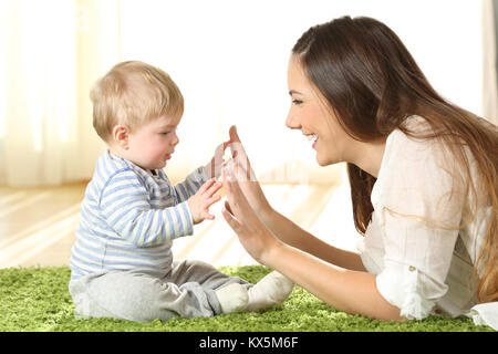 Vue latérale du portrait d'une mère heureuse de jouer avec son bébé de toucher les mains sur un tapis à la maison Banque D'Images