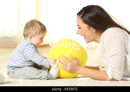 Vue latérale du portrait d'une mère heureuse de jouer avec son bébé avec une balle se trouvant sur le plancher à la maison Banque D'Images