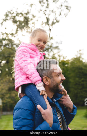 Smiling little girl riding sur le père est de retour dans le parc Banque D'Images