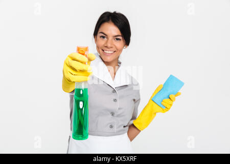 Close-up portrait of professional gouvernante en uniforme jaune et des gants en caoutchouc de pulvériser le nettoyant sur vous, isolé sur fond blanc Banque D'Images