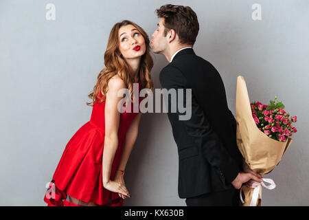 Portrait d'un jeune couple charmant tandis que debout et tenant bouquet sur fond de mur gris Banque D'Images