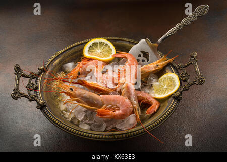 Grandes Crevettes tiger et tranche de citron frais dans l'ancienne assiette pleine de glace sur fond sombre Banque D'Images