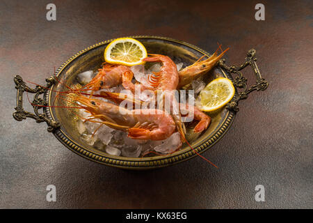 Grandes Crevettes tiger et tranche de citron frais dans l'ancienne assiette pleine de glace sur fond sombre Banque D'Images