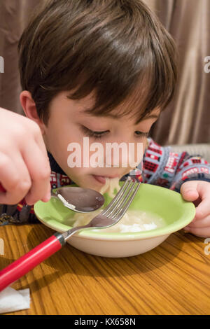 Un jeune garçon est assis à la table de la salle à manger et mange un bol de nouilles instantanées soupy. Banque D'Images