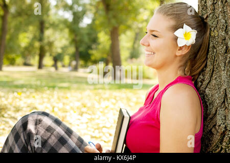 Smiling student girl sitting in park next tree Banque D'Images