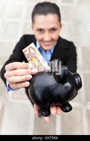 Pretty woman holding a Piggy Bank et de mettre de l'argent, (accent sur la tirelire), vue du dessus Banque D'Images