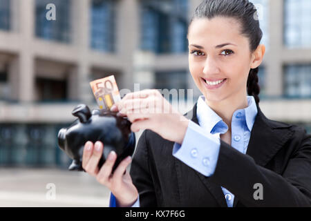 Woman putting money in piggy bank, extérieur Banque D'Images