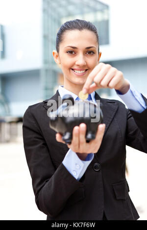 Businesswoman putting coins in piggy bank d'argent devant son immeuble de bureaux Banque D'Images