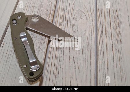 Un couteau de poche pliant ouvert avec une poignée verte portant sur une table en bois blanc Banque D'Images