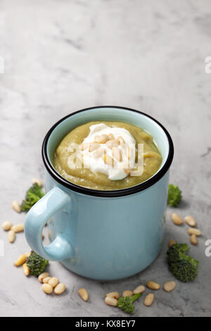 Soupe crème de brocoli au fromage à la crème et les noix de pin dans une tasse bleue sur un fond de béton gris Banque D'Images