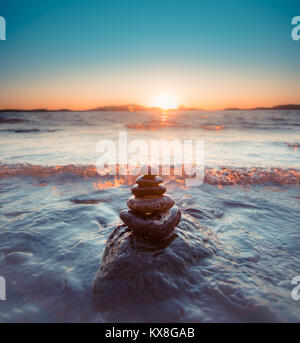 Des pierres lisses pyramide ronde en forme par la mer avec des vagues qui se présentent durant le coucher du soleil d'or Banque D'Images