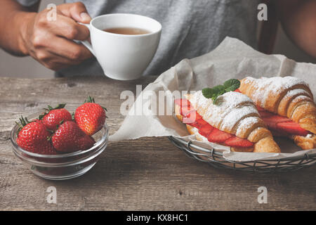 Croissant et de fraises fraîches, de ricotta (fromage blanc) pour le petit-déjeuner sur un fond de bois. Man holding tasse de café Banque D'Images