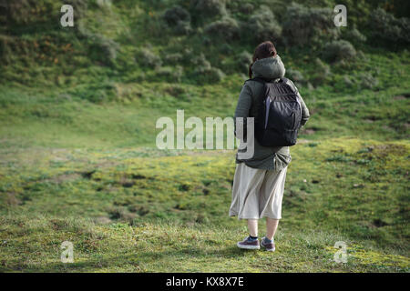 Une jeune femme de race blanche debout sur une colline herbeuse par elle-même avec un sac à dos et une longue jupe sur à la recherche dans la distance prêt à explorer le réseau local Banque D'Images