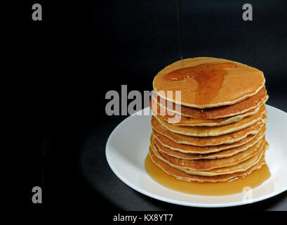 Pile de crêpes fraîches faites maison avec du sirop servi sur assiette blanche, fond noir avec de l'espace libre pour le texte ou dessin Banque D'Images