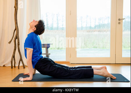 Man practicing yoga à l'intérieur dans un espace de réflexion faisant du cobra posent - urdhva mukha svanasana Banque D'Images