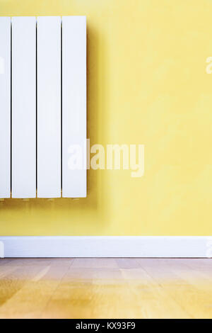 Blanc moderne radiateur électrique avec thermostat électronique installé dans une chambre avec parquet au sol, mur jaune et blanc plinthe. Banque D'Images