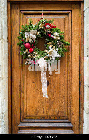 Vue frontale d'une couronne de Noël traditionnel fait de branches d'arbre de pin rouge, des boules de Noël et houx Feuilles et baies accrochées sur une porte en bois. Banque D'Images