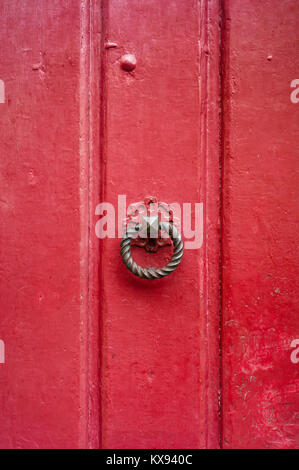 Vue frontale d'un round et fonte torsadée heurtoir monté sur une vieille porte en bois peinte en rouge. Banque D'Images