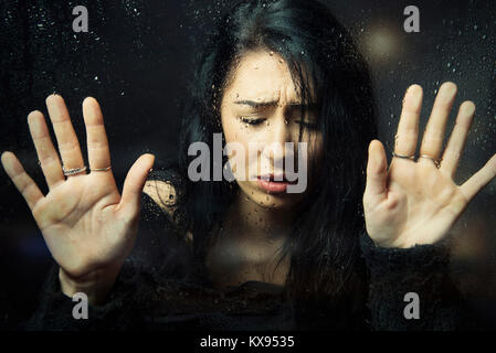 Distressed triste déprimé malheureux femme mains pressées contre le bas de la fenêtre à la fenêtre à rainy closeup portrait cinématographique Banque D'Images