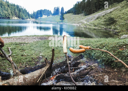 Des bâtons en griller les saucisses sur le barbecue cheminée en face de lac de montagne Banque D'Images