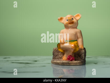 Figurine d'un petit cochon assis sur un banc, fond vert Banque D'Images