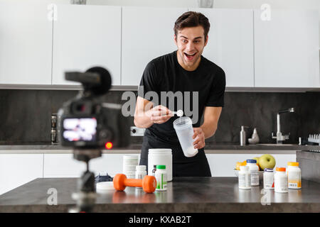 Jeune homme excité de filmer son blog vidéo épisode sur les additifs alimentaires sains tout en se tenant à la table de cuisine Banque D'Images