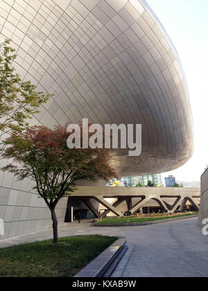 Vue partielle d'un bâtiment futuriste dans la conception de Dongdaemun Plaza, un patch d'herbe verte et un arbre à feuilles rouges, à Séoul, Corée du Sud Banque D'Images