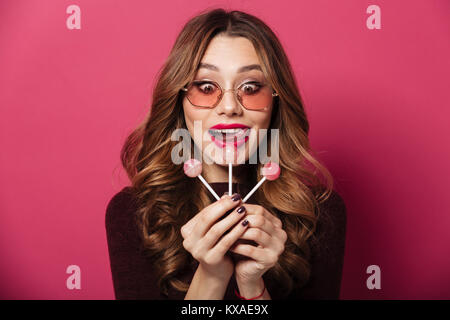 Photo de jeune femme exceptionnelle portant des lunettes isolés sur fond rose. À côté d'un grand nombre de sucreries. Banque D'Images