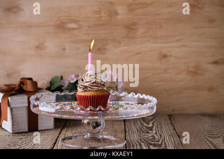 Delicious birthday cupcake avec une bougie servi sur du verre sur table en bois fête cakestand Banque D'Images