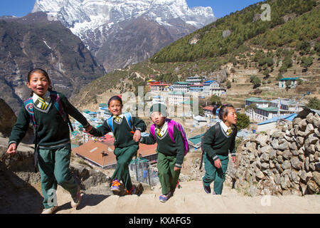 Quatre jeunes enfants vêtus de l'uniforme est la marche en montagne Namche Bazar, un village de montagne dans la vallée du Khumbu au Népal. Banque D'Images