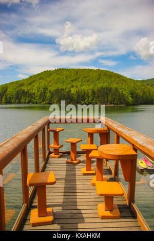 Paysage de montagne avec une terrasse en bois avec chaises et tables sur le lac Gozna entouré par la forêt, Valiug, Caras-Severin, Roumanie Banque D'Images