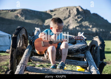 Garçon mongol à jouer de la guitare tout en restant assis sur le yak panier, Bunkhan, Bulgan, Mongolie Banque D'Images