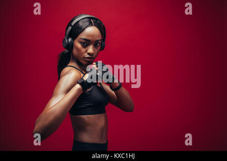 Femme noire difficiles avec un casque en position de combat permanent. African boxer exerçant sur fond rouge Banque D'Images