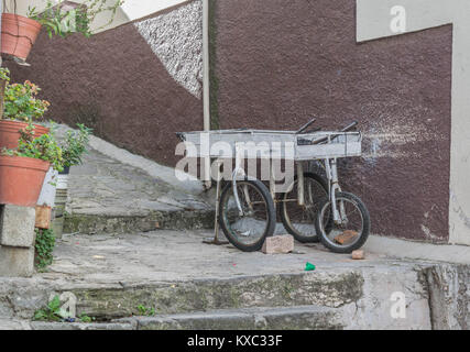 Un petit panier blanc avec trois roues pneumatiques, sur un sentier en pierre avec quelques plantes en pot et un mur avec peinture mauve, à Guanajuato, Mexique Banque D'Images